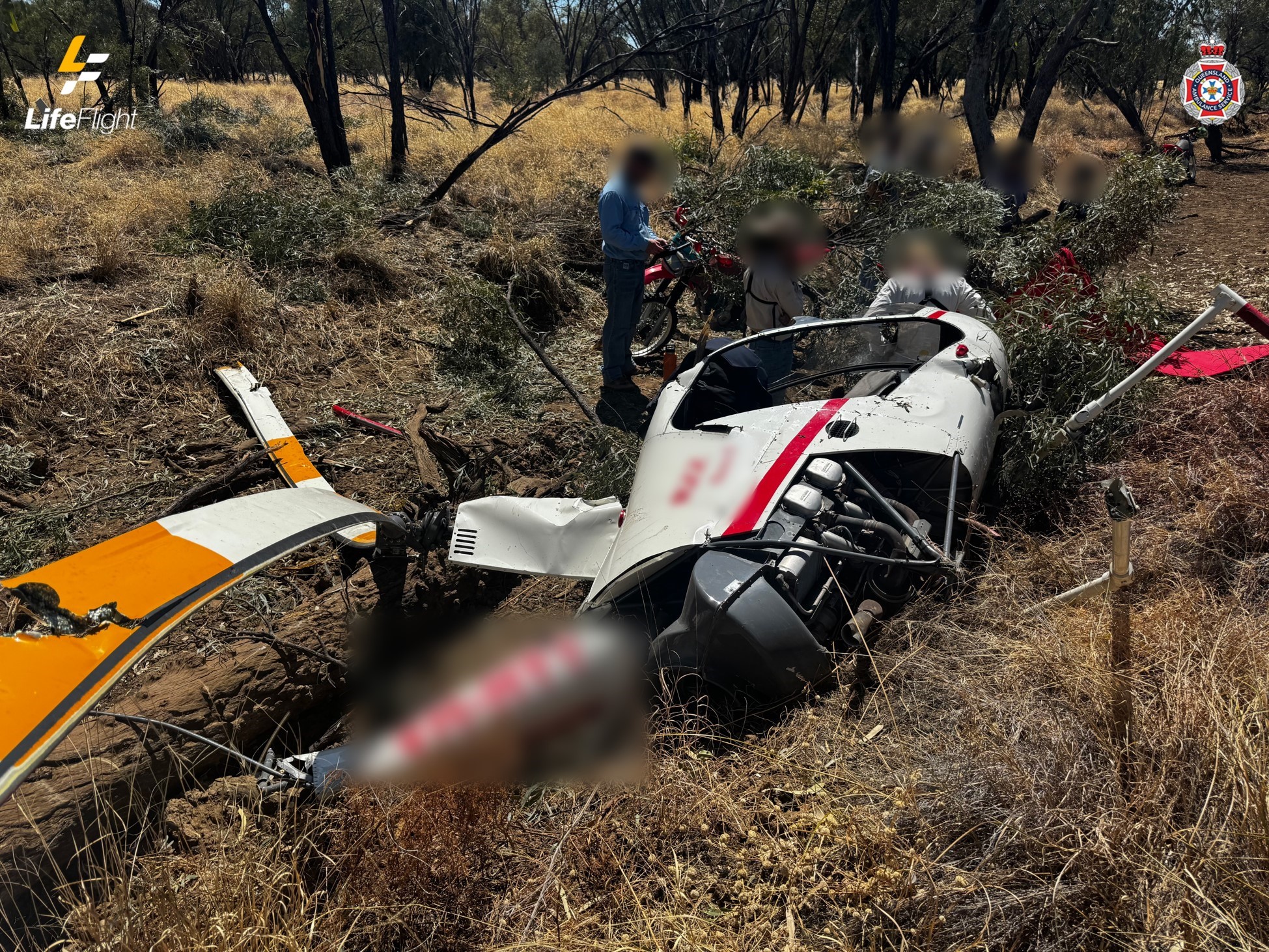 Robinson R22 on its left side in a dry creek bed. The image shows damage to the fuselage and main rotor system. The tail rotor assembly was removed in the accident sequence.