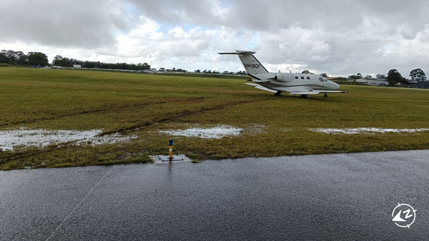 The aircraft in muddy ground off the end of the runway.