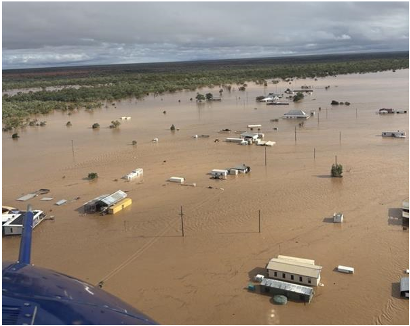 Overhead picture of Adavale after the accident taken from a helicopter, showing widespread flooding of the town and broken low level cloud. Multiple powerlines are visible along the flooded streets.