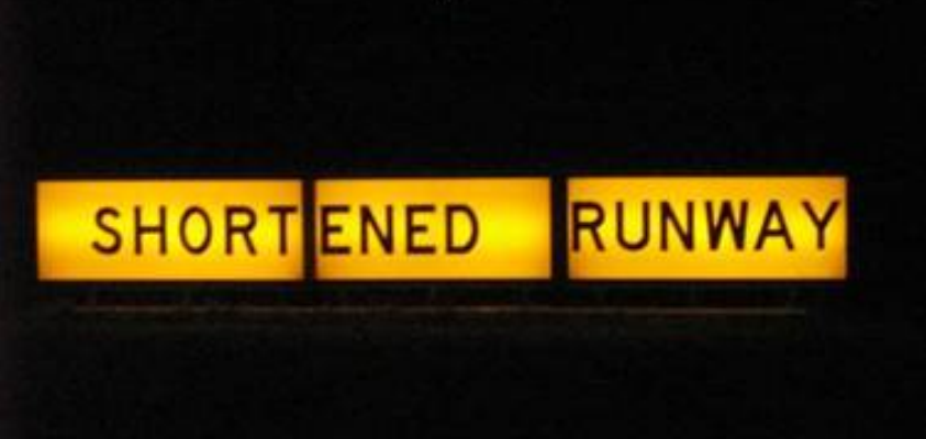 A backlit sign with black text on a yellow background. The text reads 'shortened runway' across three panels.