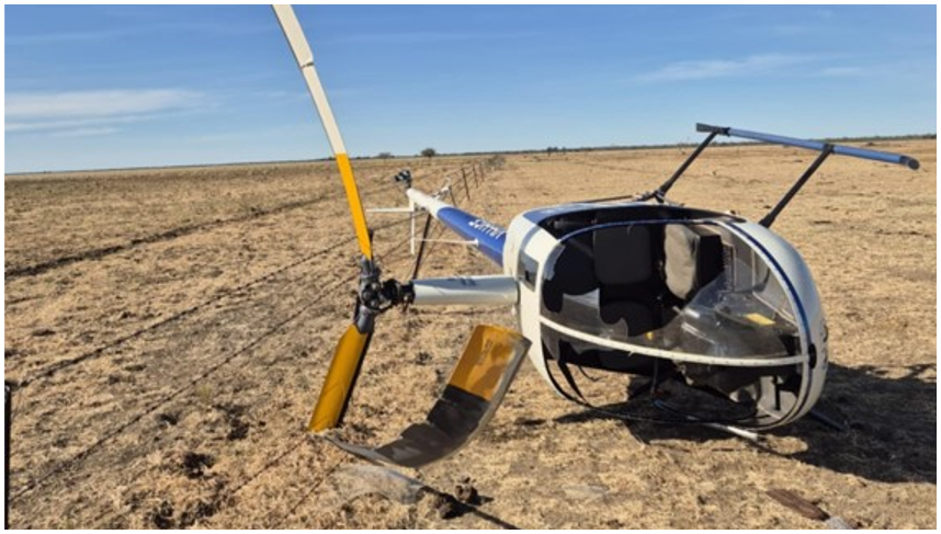 Robinson R22 VH-HGE on its right side with visible damage to the main rotor blades and windshield.