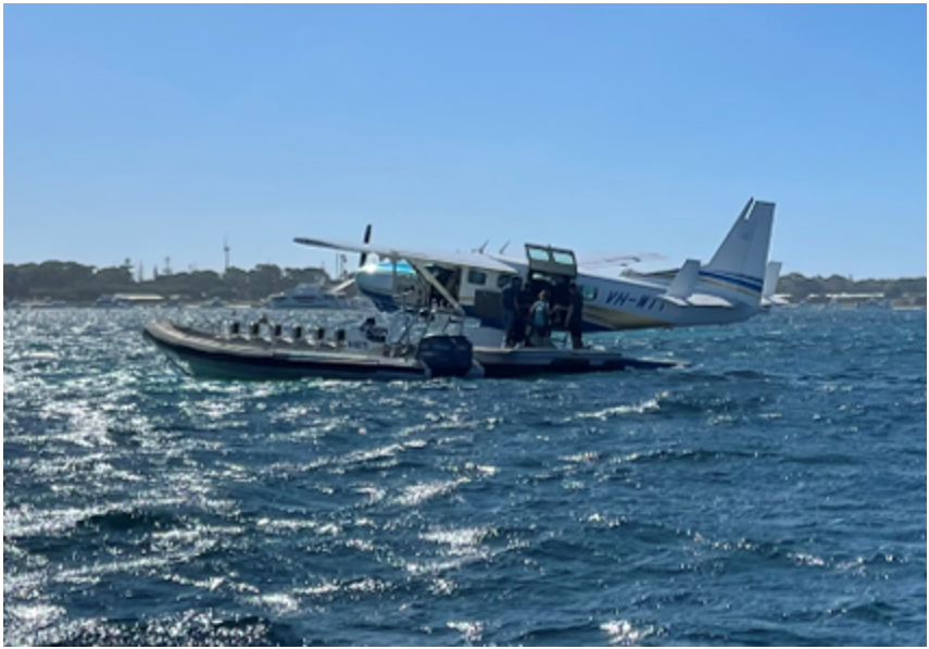 An image of the C208 floatplane registered VH-WTY. The aircraft is on the water with a boat docked alongside. 