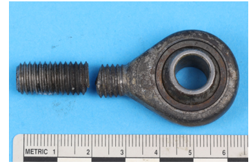 Photograph of the fractured NLG actuator rod, pictured against a ruler to show the size.