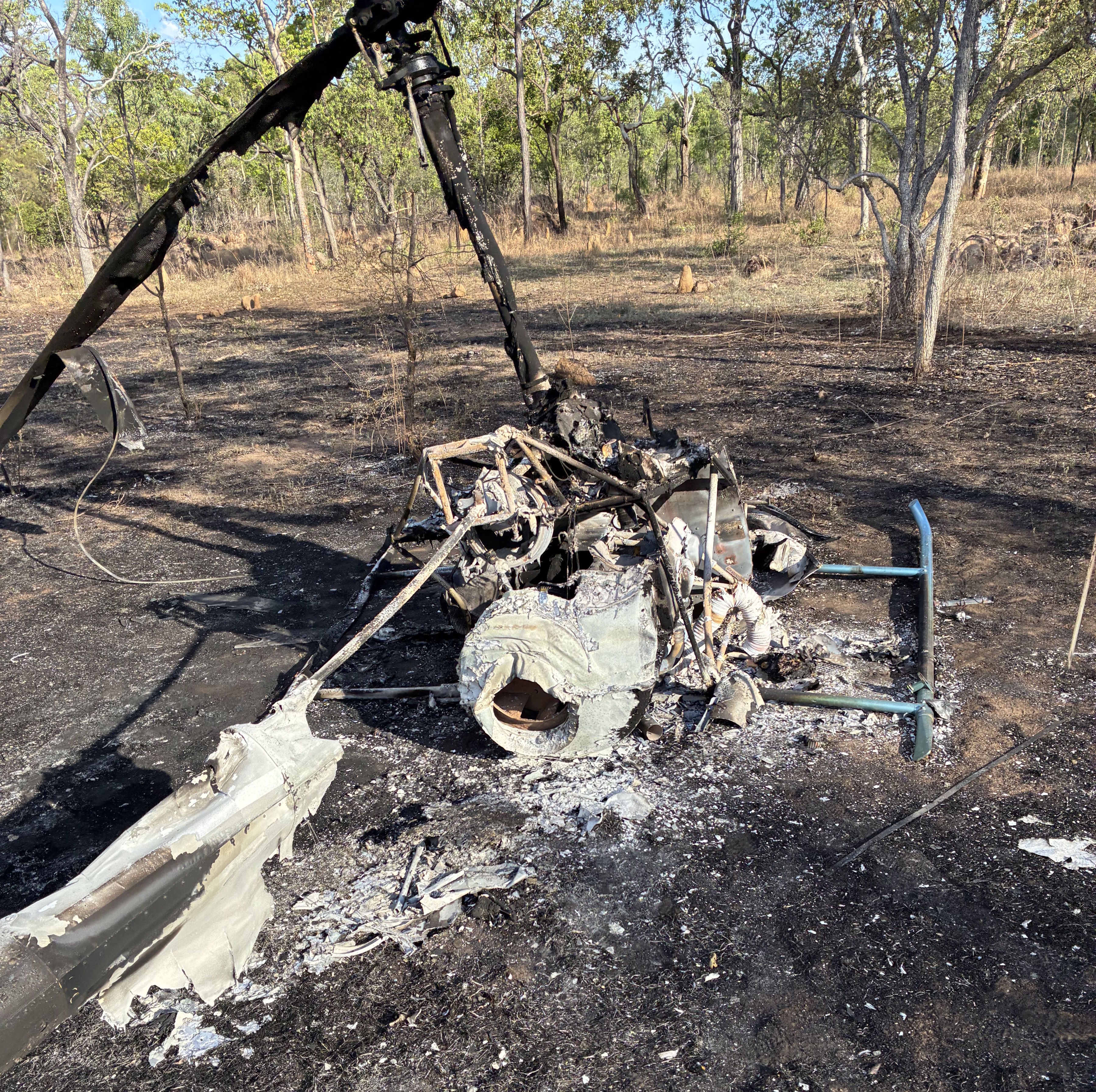 Completely burnt helicopter, pictured from the rear. Skids are spread flat, parallel to the ground. Area around the helicopter also burnt.