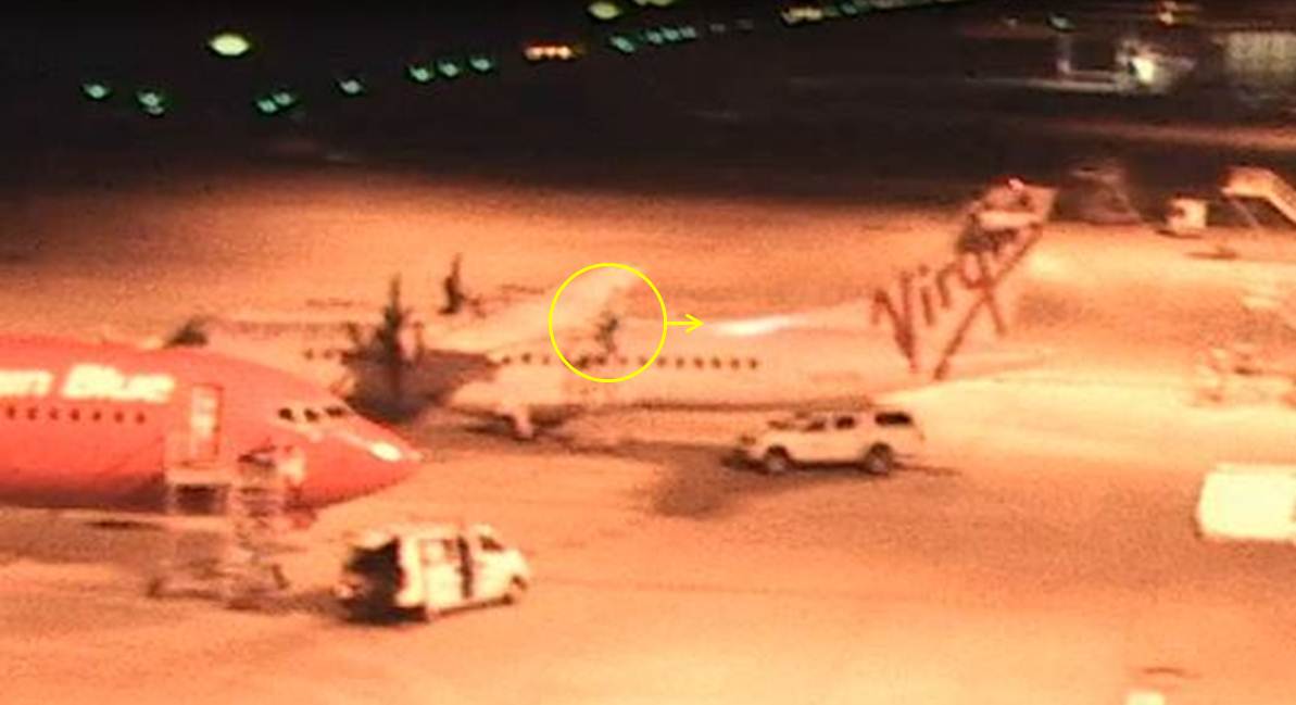 Figure 3: Aircraft visual inspection underway at 2306:44 with LAME 2 on the stand at the rear of the left wing. The circle and arrow indicate the location of the LAME and the direction of torchlight (still image copied from closed circuit TV footage)