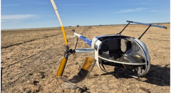 Robinson R22 VH-HGE on its right side with visible damage to the main rotor blades and windshield.