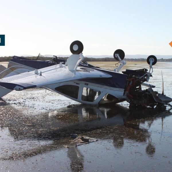 Accident site photo showing VH-WMM inverted on the tidal flat at low tide. The direction of travel and location of Redcliffe airfield are also noted.