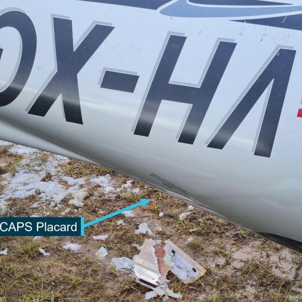 Wreckage (inverted) at accident site showing CAPS warning placard on left rear fuselage
