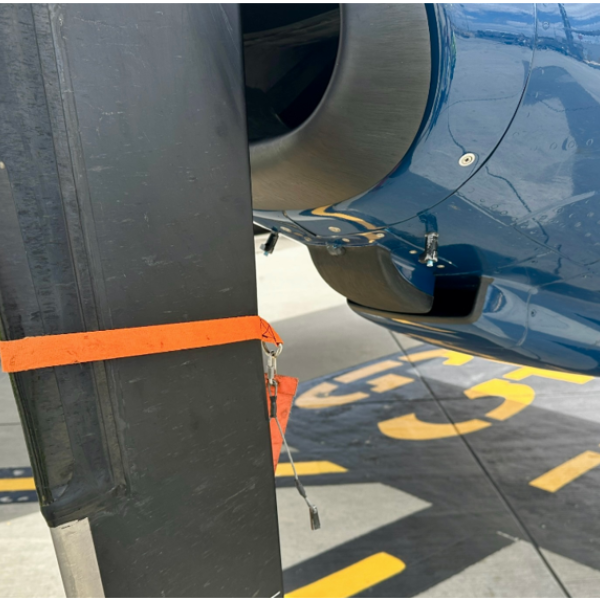 Image of an aircraft propeller blade and engine cowling. The propeller blade has an orange strap attached to it, and the engine cowling has pins attached.