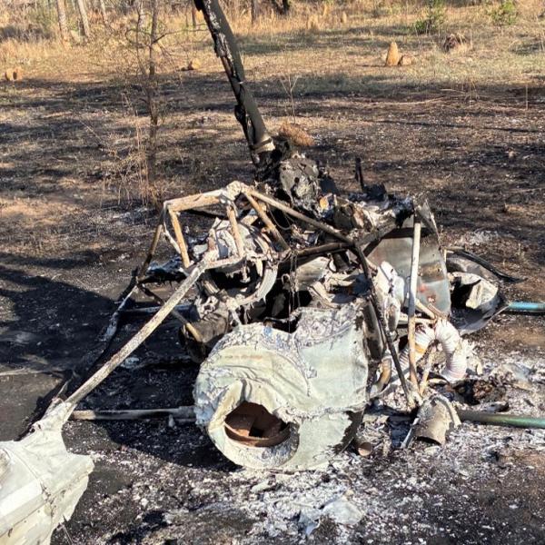 Completely burnt helicopter, pictured from the rear. Skids are spread flat, parallel to the ground. Area around the helicopter also burnt.